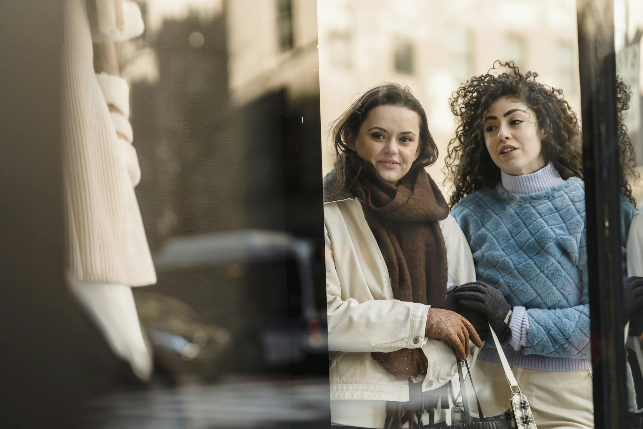 Through glass of stylish young multiracial ladies in trendy warm clothes standing near fashion boutique showcase and choosing clothes